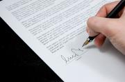 Closeup of person's hand holding pen and signing document.